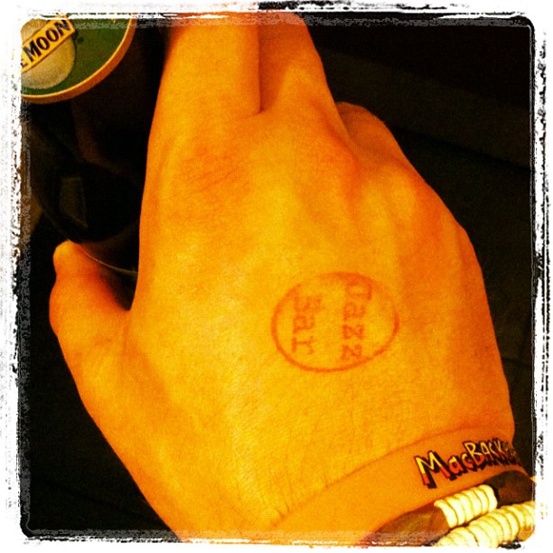 Hand holding a bottle, with a circular ink stamp on the back and bracelets on the wrist.