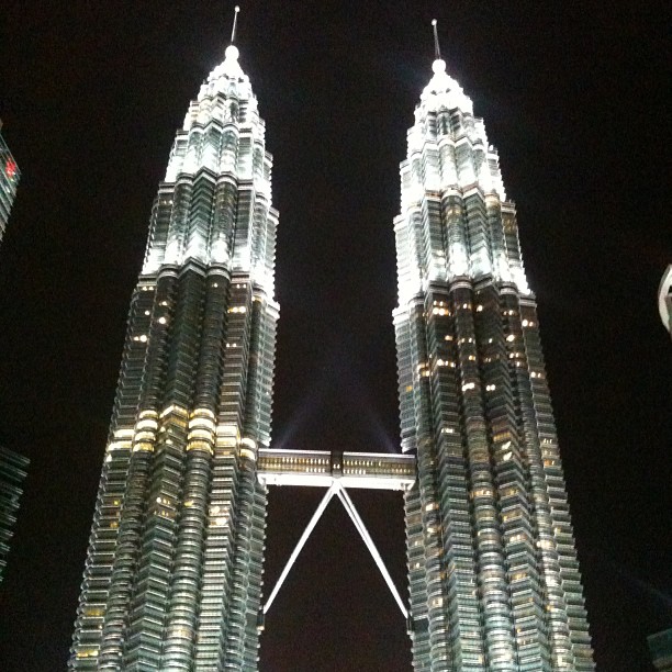 Two illuminated twin skyscrapers at night connected by a skybridge against a dark sky.