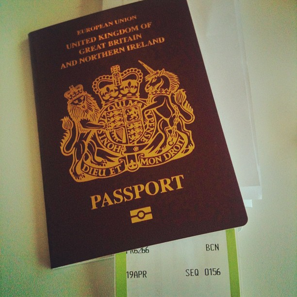 United Kingdom passport with gold crest and text, resting on top of a partially visible boarding pass.