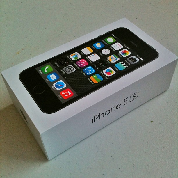 White iPhone 5s box on a table, showing the phone with app icons on the lid and "iPhone 5s" printed on the side.