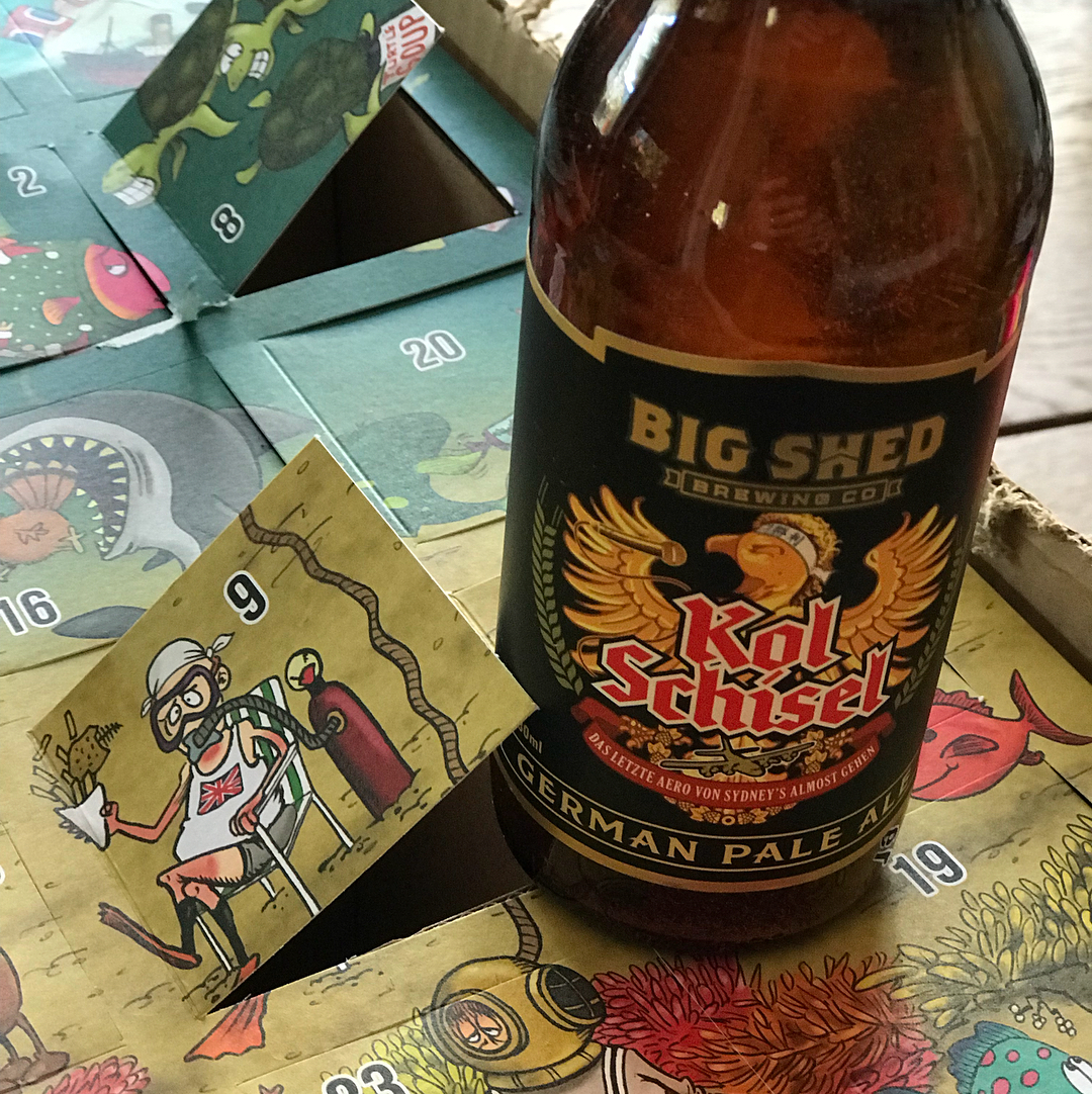 Bottle of Big Shed Kol Schisel German Pale Ale on a colorful illustrated board with numbered flaps, including an open flap marked 9.