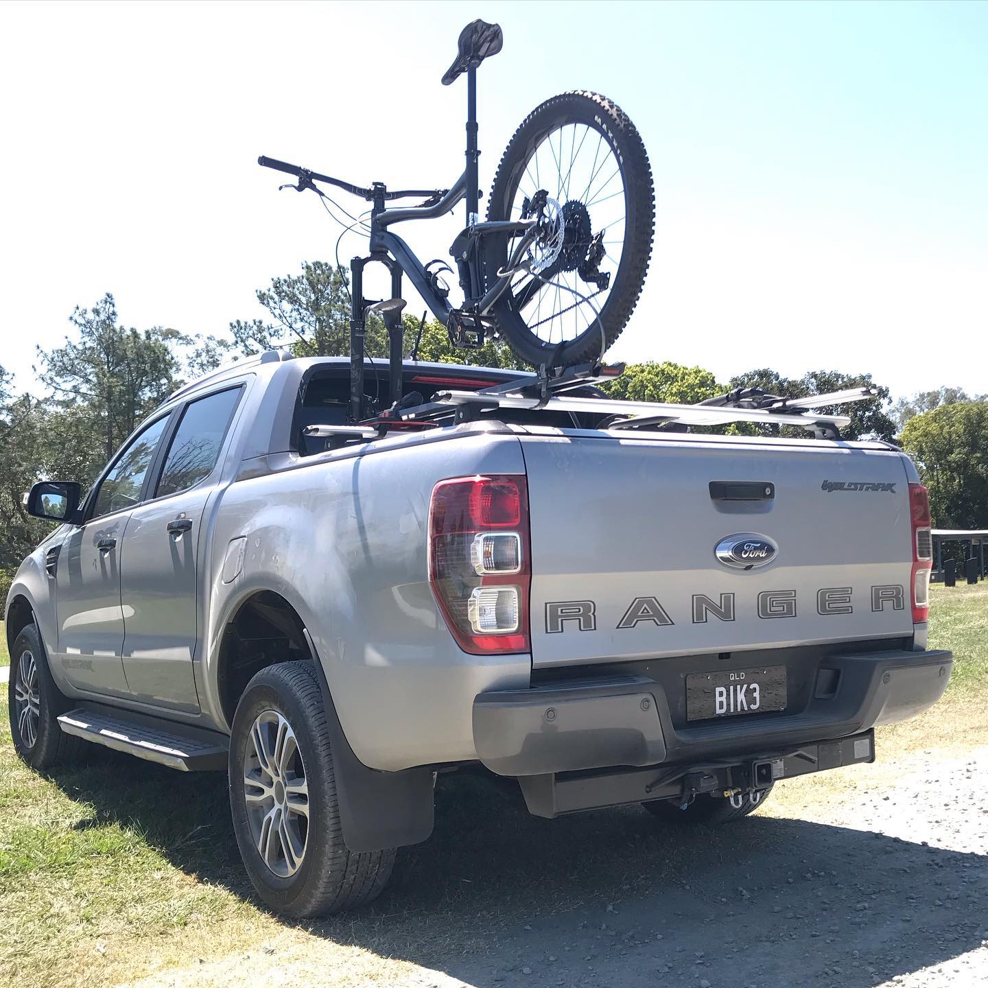 Silver pickup truck parked on grass with a mountain bike mounted upright on racks over the truck bed.