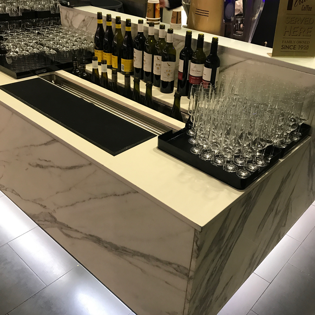 Marble bar counter with rows of wine bottles, stacked glassware, and trays of empty champagne flutes.