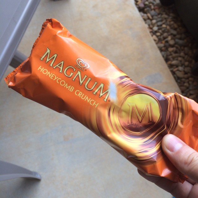 Hand holding a wrapped Magnum Honeycomb Crunch ice cream bar in orange packaging.