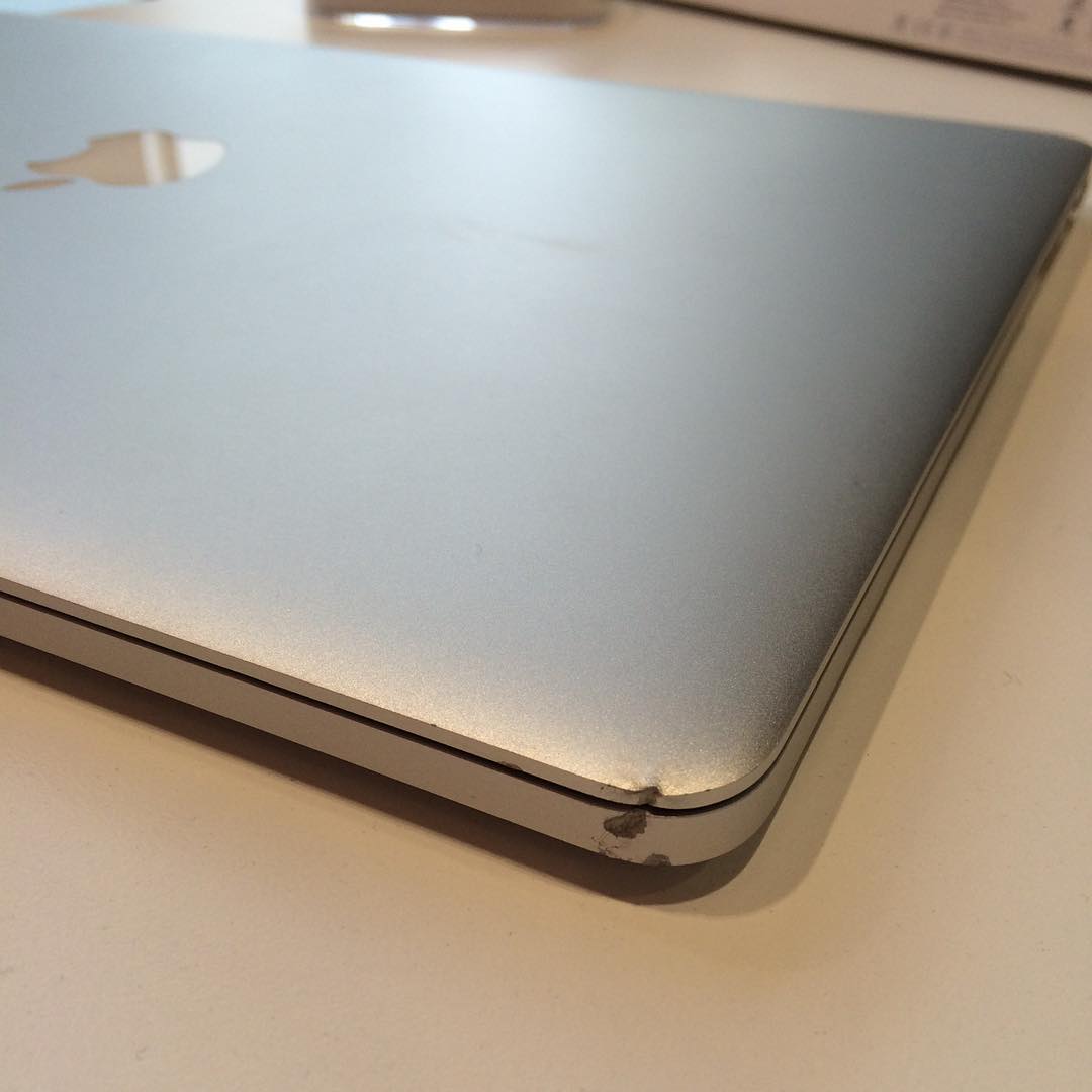 Close-up of a silver laptop with visible denting and chipped metal on one corner.