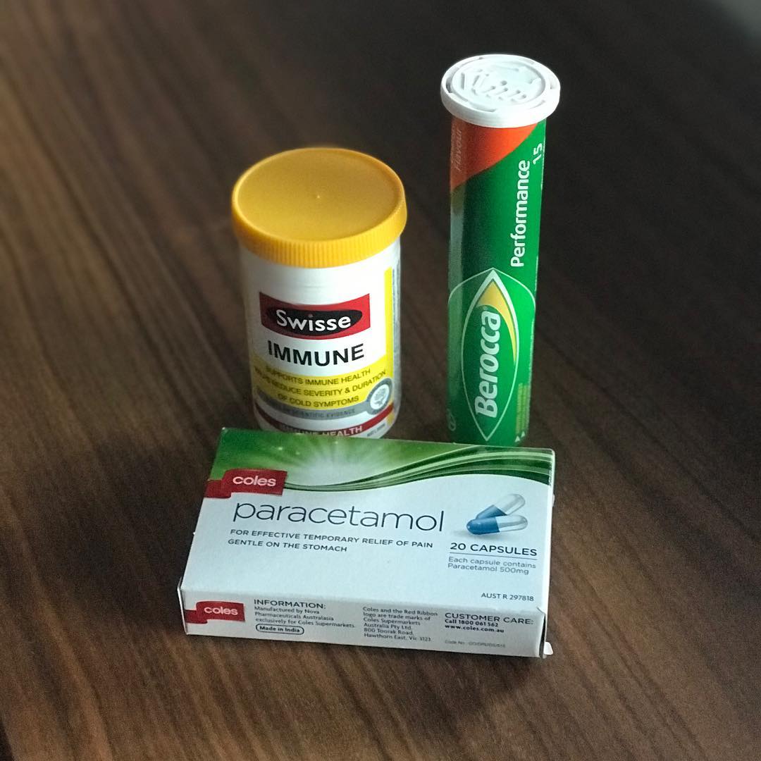 Box of paracetamol capsules beside tubes of Swisse Immune and Berocca Performance tablets on a wooden table.
