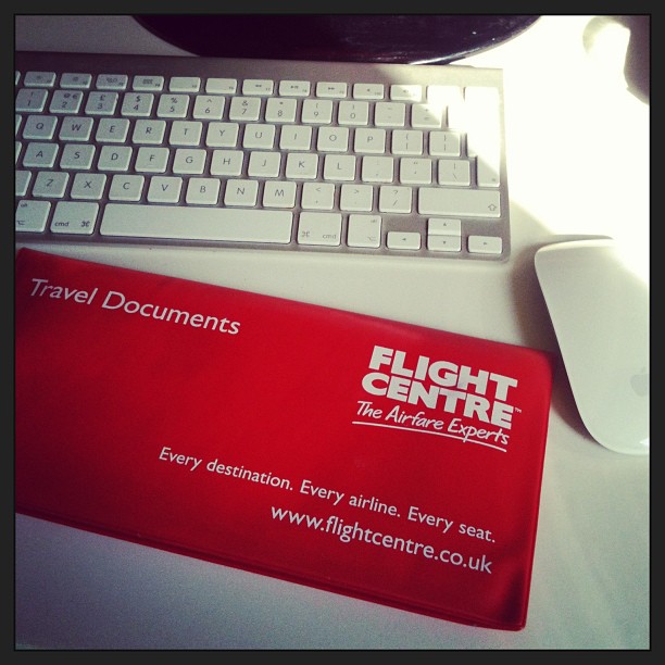 Red travel document wallet on a desk beside a white keyboard and mouse.