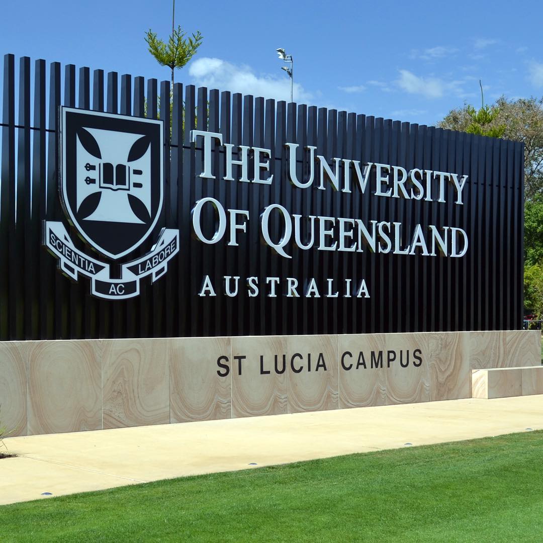 Sign for The University of Queensland Australia at St Lucia Campus, with crest on a black slatted wall under a blue sky.