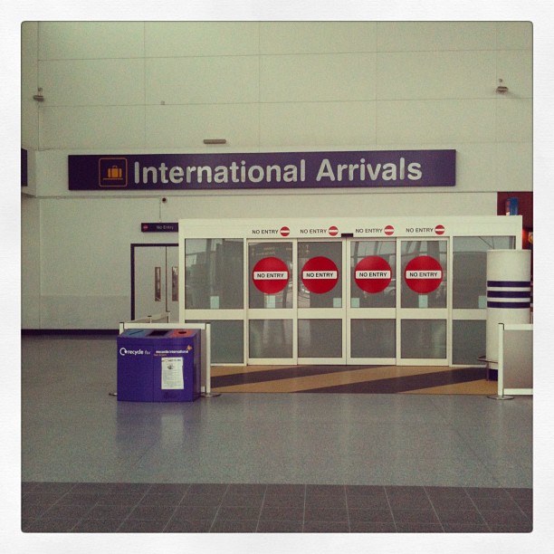 International Arrivals sign above closed glass doors marked with multiple No Entry symbols in an airport terminal.
