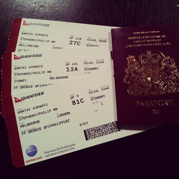 Three Qantas boarding passes beside a burgundy British passport on a dark wooden surface.