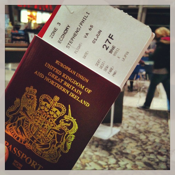UK passport holding a boarding pass with seat 27F in an airport terminal.