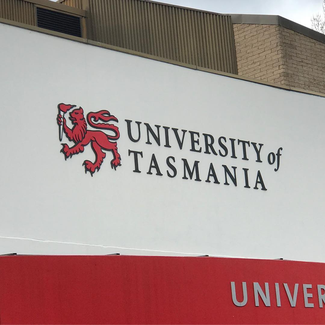 University of Tasmania sign with a red lion emblem on a white wall above a red panel.