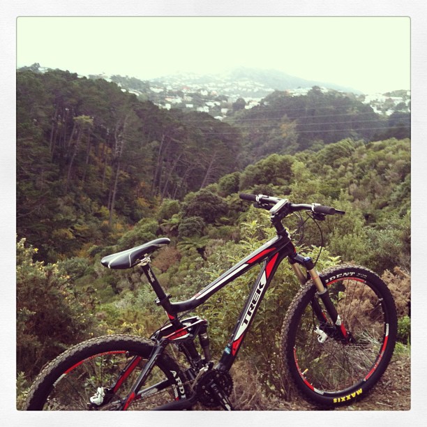 Black and red mountain bike on a dirt overlook with dense green hills and a misty town in the background.