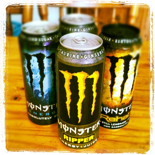 Four Monster Energy drink cans on a wooden table, with the front can labeled Ripper.
