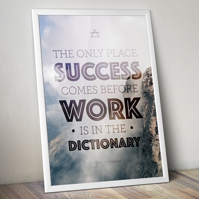 Framed poster on a wooden surface with the quote “The only place success comes before work is in the dictionary” over a mountain scene.