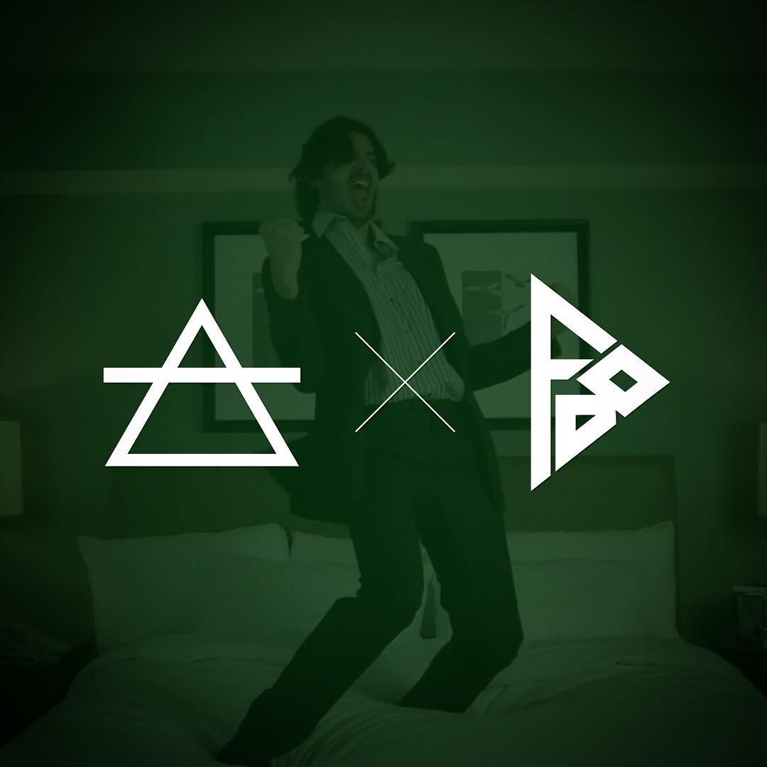 Person in a suit jumping on a bed with large white geometric symbols over a dark green-tinted background.