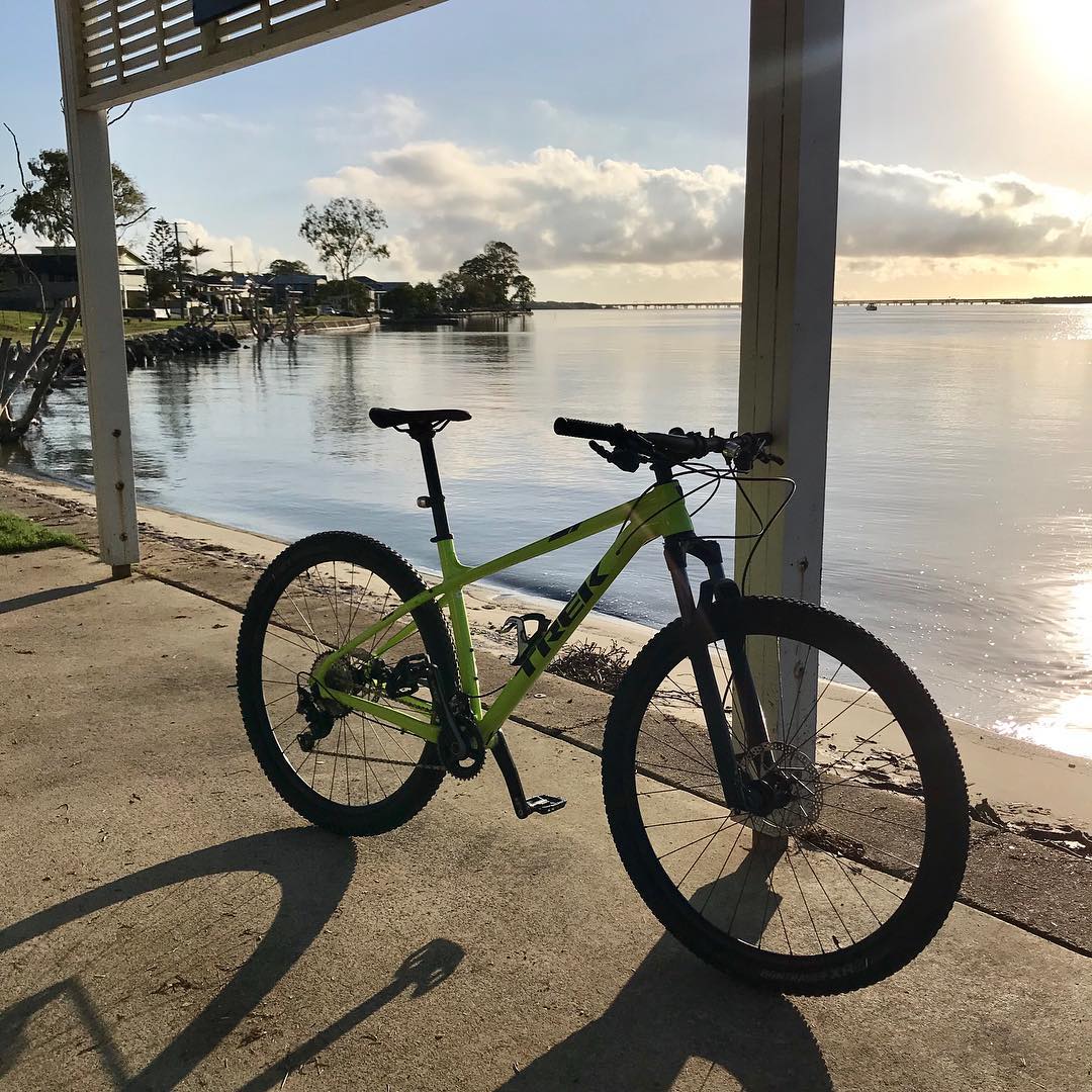 Green mountain bike on a concrete shore under a shelter beside calm water at sunset.