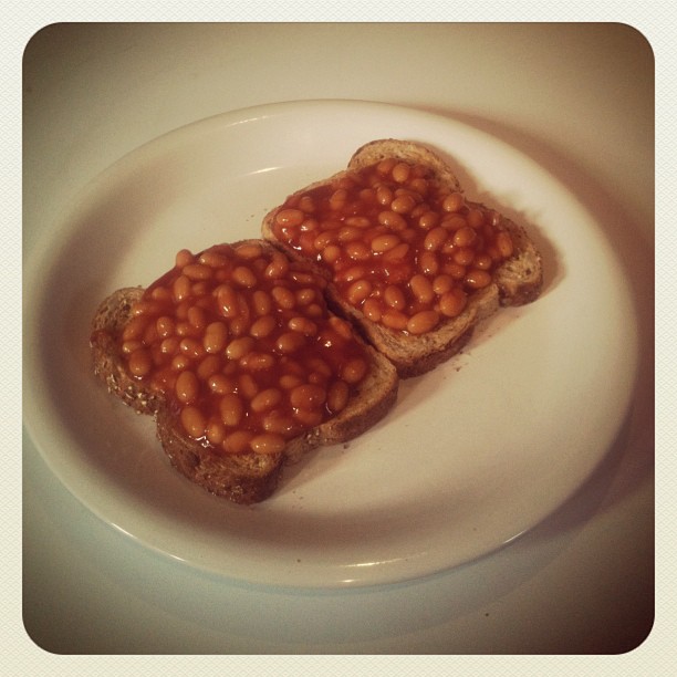 Two slices of toast topped with baked beans on a white plate.