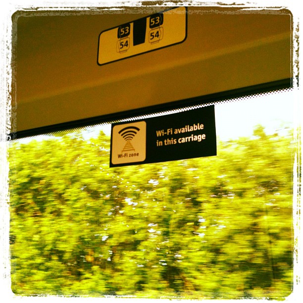 Wi‑Fi available in this carriage sign hanging above a train window, with blurred green trees outside.