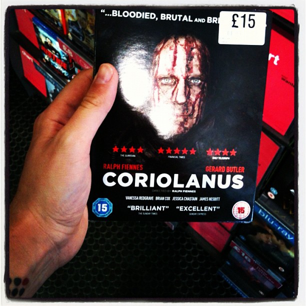 Hand holding a Coriolanus DVD case with a £15 price sticker and a blood-streaked face on the cover.