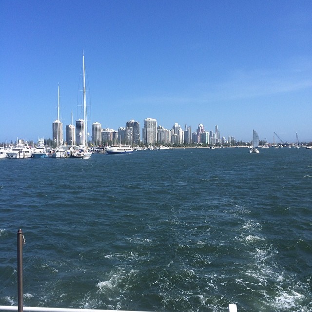 City skyline across choppy blue water, with sailboats and yachts under a clear sky.
