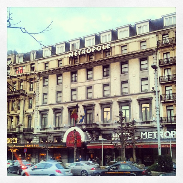 Facade of the Metropole hotel with large rooftop sign, flags above the entrance, and cars on the street in front.