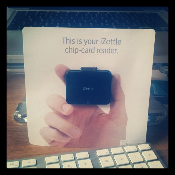 Cardboard display showing a hand holding a black iZettle chip card reader, with a keyboard and laptop in the background.