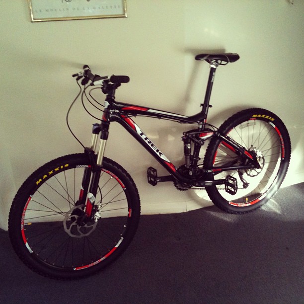 Black and red mountain bike leaning against a white wall on a dark carpet.