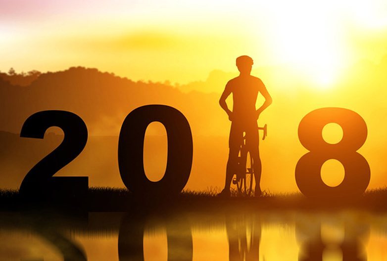 Silhouette of a person with a bicycle standing between large numbers 2, 0, and 8 at sunrise with a water reflection.