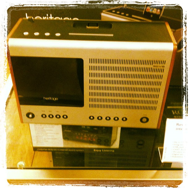 Retro tabletop radio with a dark screen, perforated speaker grille, and round control buttons on display.