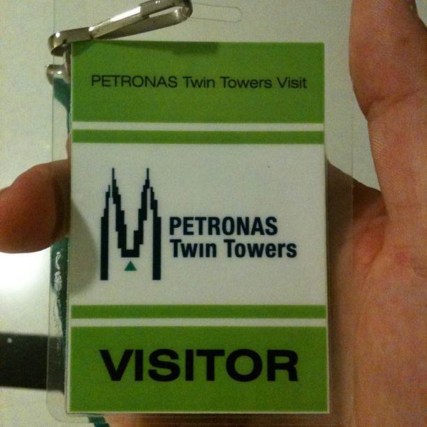 Hand holding a PETRONAS Twin Towers visitor badge in a clear plastic holder.