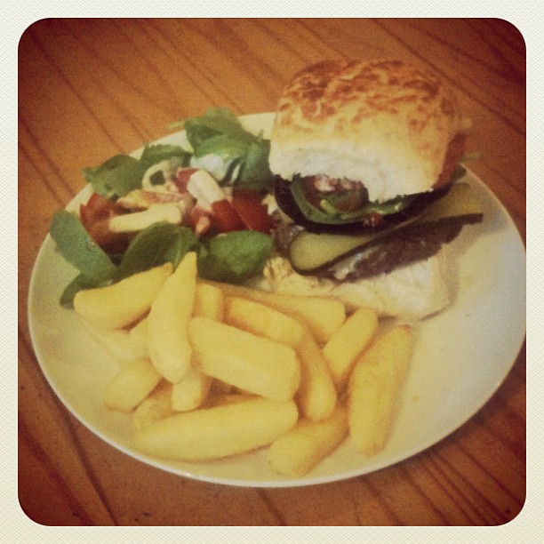 Plate with a burger, thick-cut fries, and a small side salad on a wooden table.