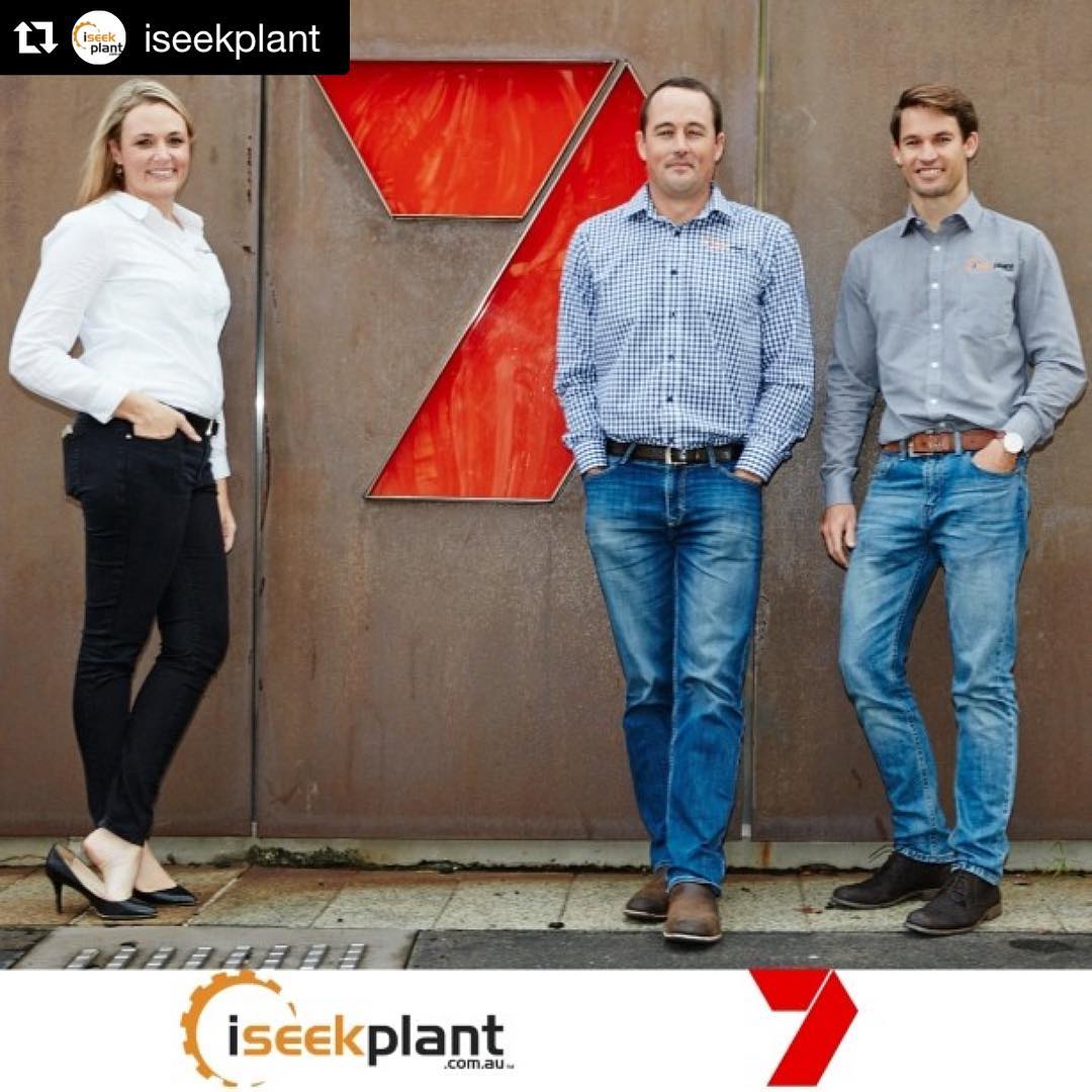 Three people standing in front of a metal wall with a large red 7 logo, with iseekplant branding at the top and bottom.