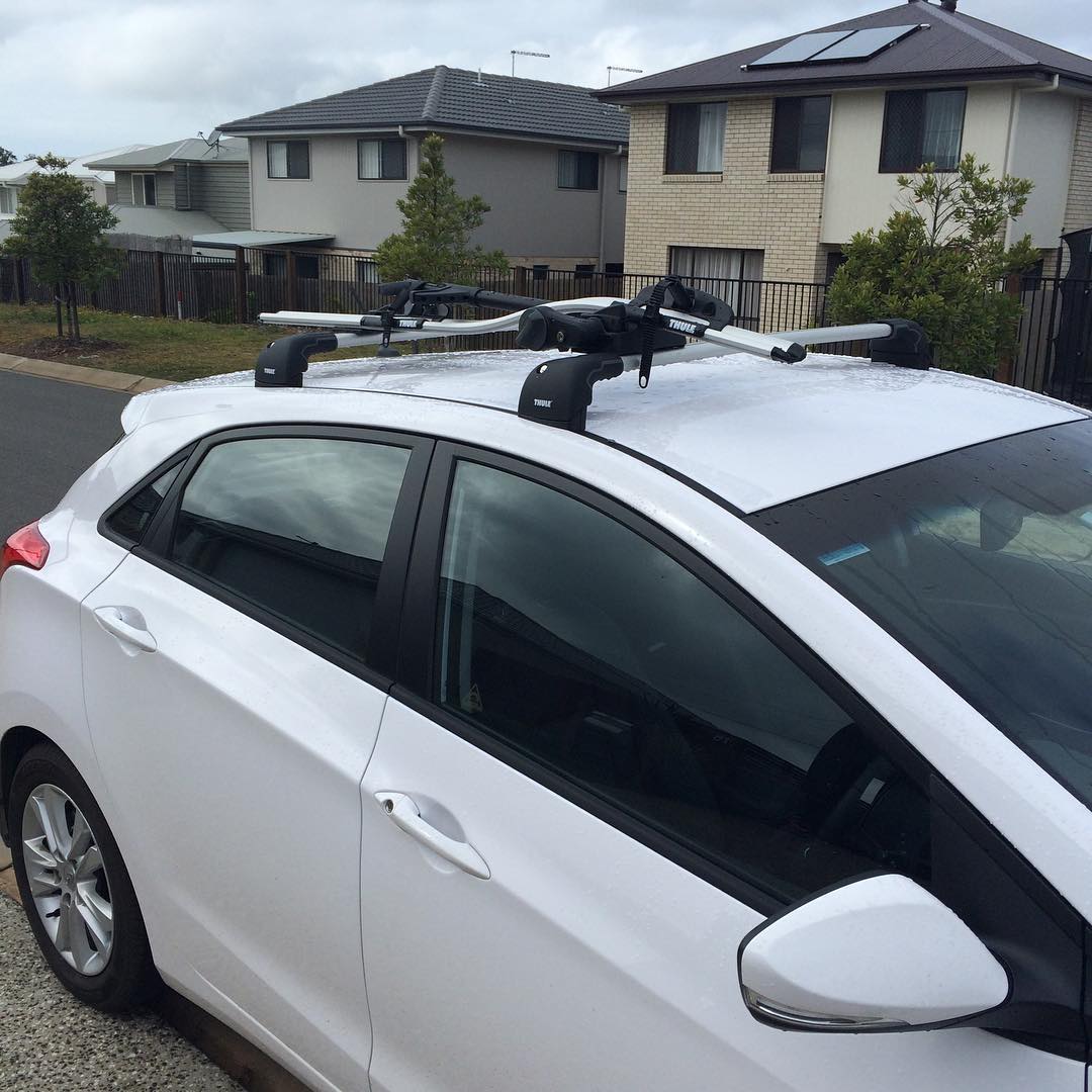 White hatchback parked on a suburban street with Thule roof racks mounted on top.