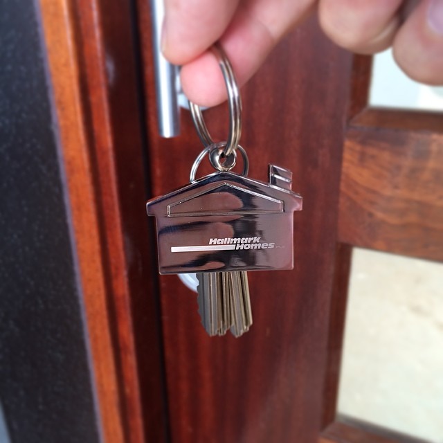 Hand holding a keyring with a house-shaped keychain and keys in a wooden door lock.