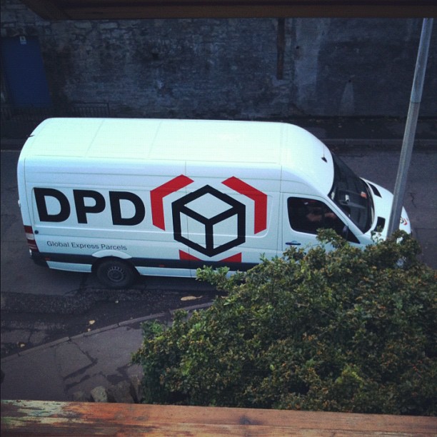 White DPD delivery van parked on a street, viewed from above, with bushes in the foreground.