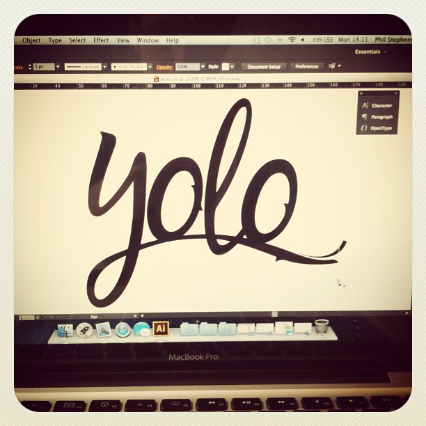 MacBook Pro screen showing Adobe Illustrator with the word “yolo” drawn in thick black script.