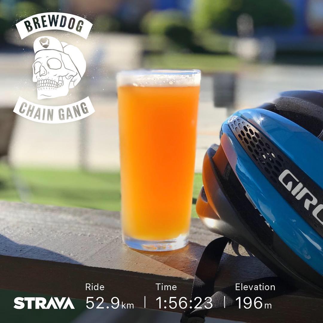 Pint of orange beer beside a blue bike helmet on a ledge, with BrewDog Chain Gang and Strava ride stats overlaid.