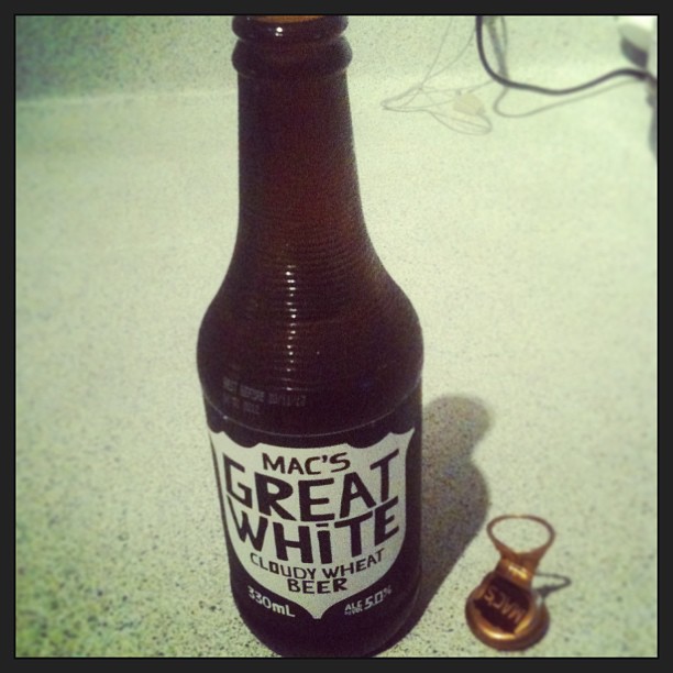 Bottle of Mac’s Great White cloudy wheat beer on a countertop beside a small copper pushpin.