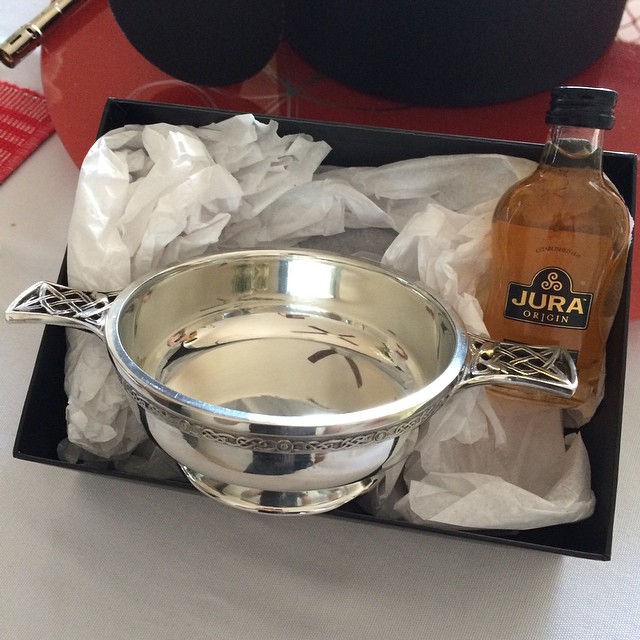 Silver bowl with ornate handles in a tissue-lined box beside a small bottle labeled Jura Origin.