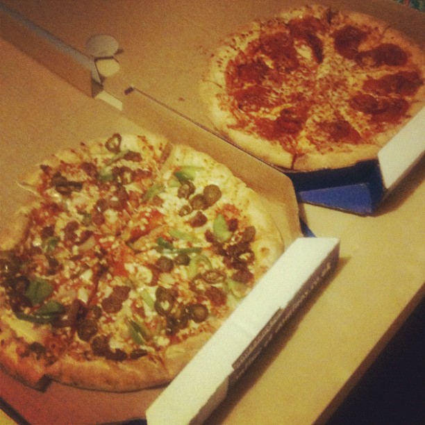 Two open pizza boxes on a table, one with a vegetable-topped pizza and one with a pepperoni pizza.