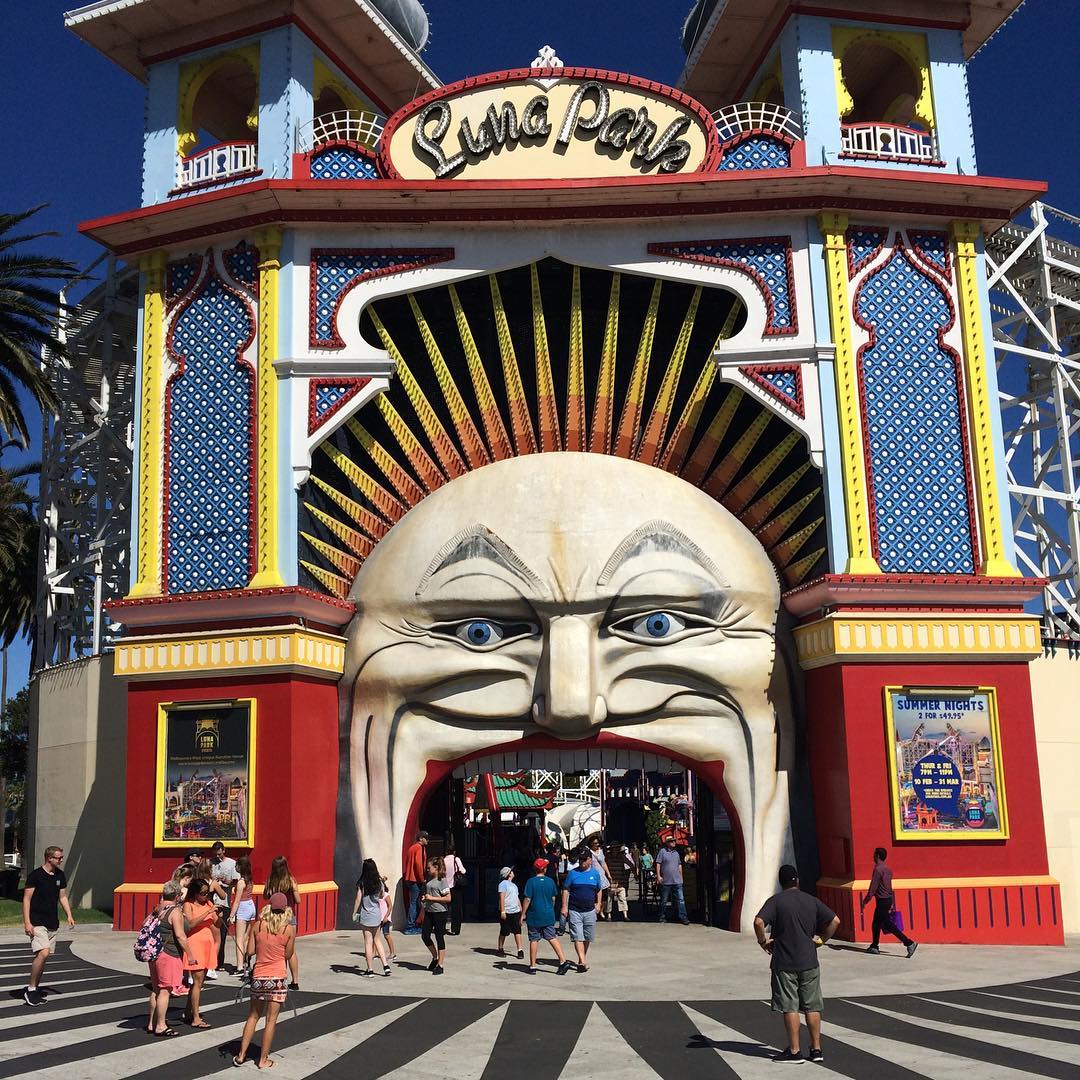 Colorful Luna Park entrance with a giant smiling face, sunburst hair, and people walking beneath its open mouth.