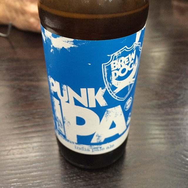 Brown beer bottle with a bright blue BrewDog Punk IPA label on a dark wooden table.