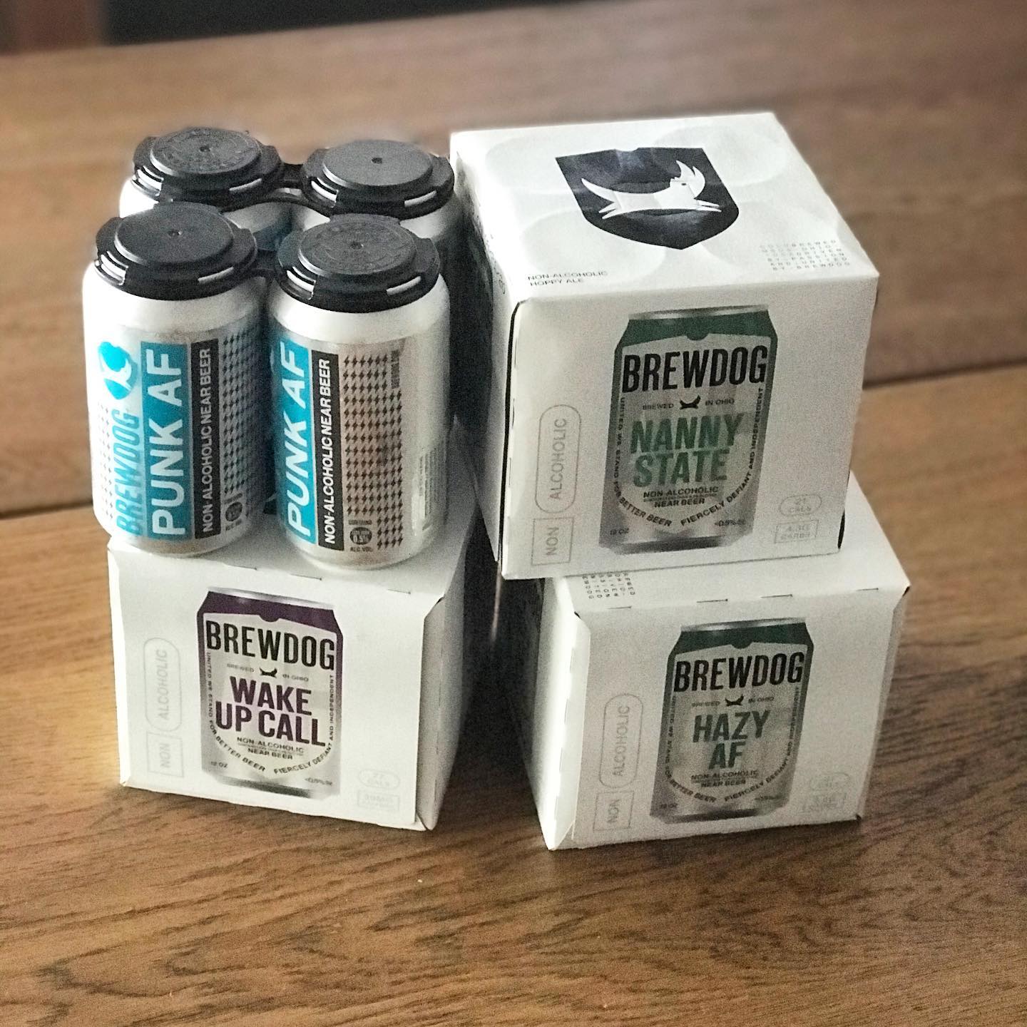 Four silver Punk AF cans and three white BrewDog nonalcoholic beer boxes stacked on a wooden table.