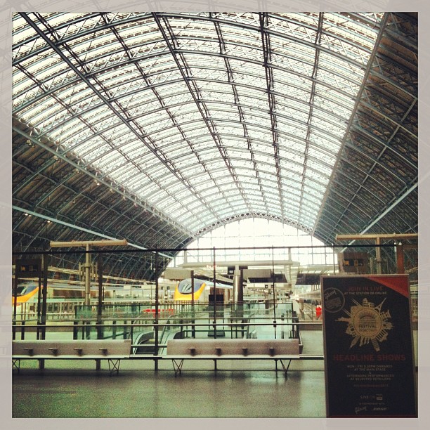 Large glass-and-steel arched train station interior with benches, platforms, and a signboard in the foreground.