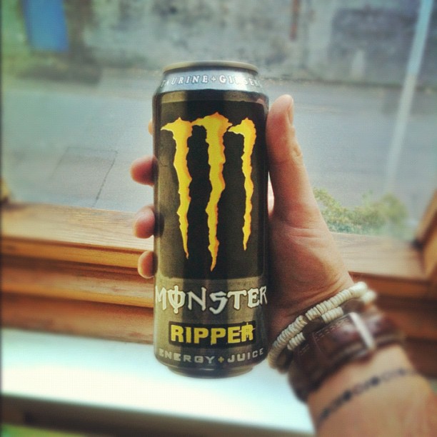 Hand holding a can of Monster Ripper energy drink by a window.