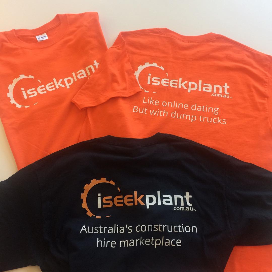Three branded T-shirts laid flat: two bright orange and one black, printed with the iseekplant logo and promotional text.