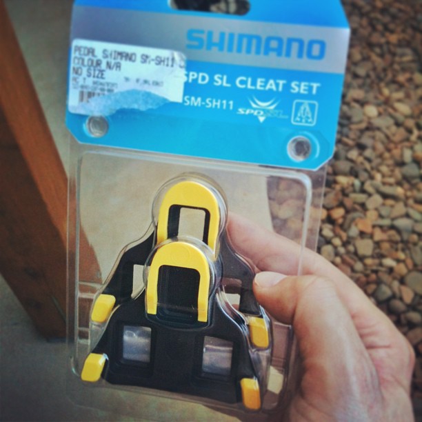 Hand holding a packaged Shimano SPD-SL cleat set with black and yellow cleats.