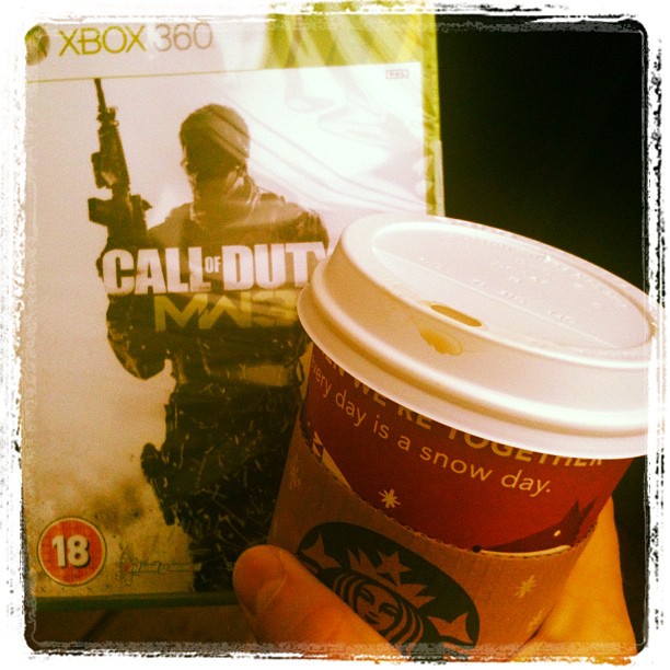 Hand holding a Starbucks coffee cup in front of an Xbox 360 Call of Duty game case.